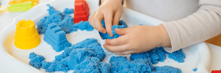 Toddler playing with blue kinetic sand and molds during sensory play activity at STEM Child Care